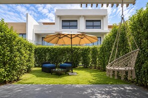 Eine moderne Außenpatio mit Schaukelstuhl, gepolsterten Sitzgelegenheiten und einem großen Sonnenschirm.