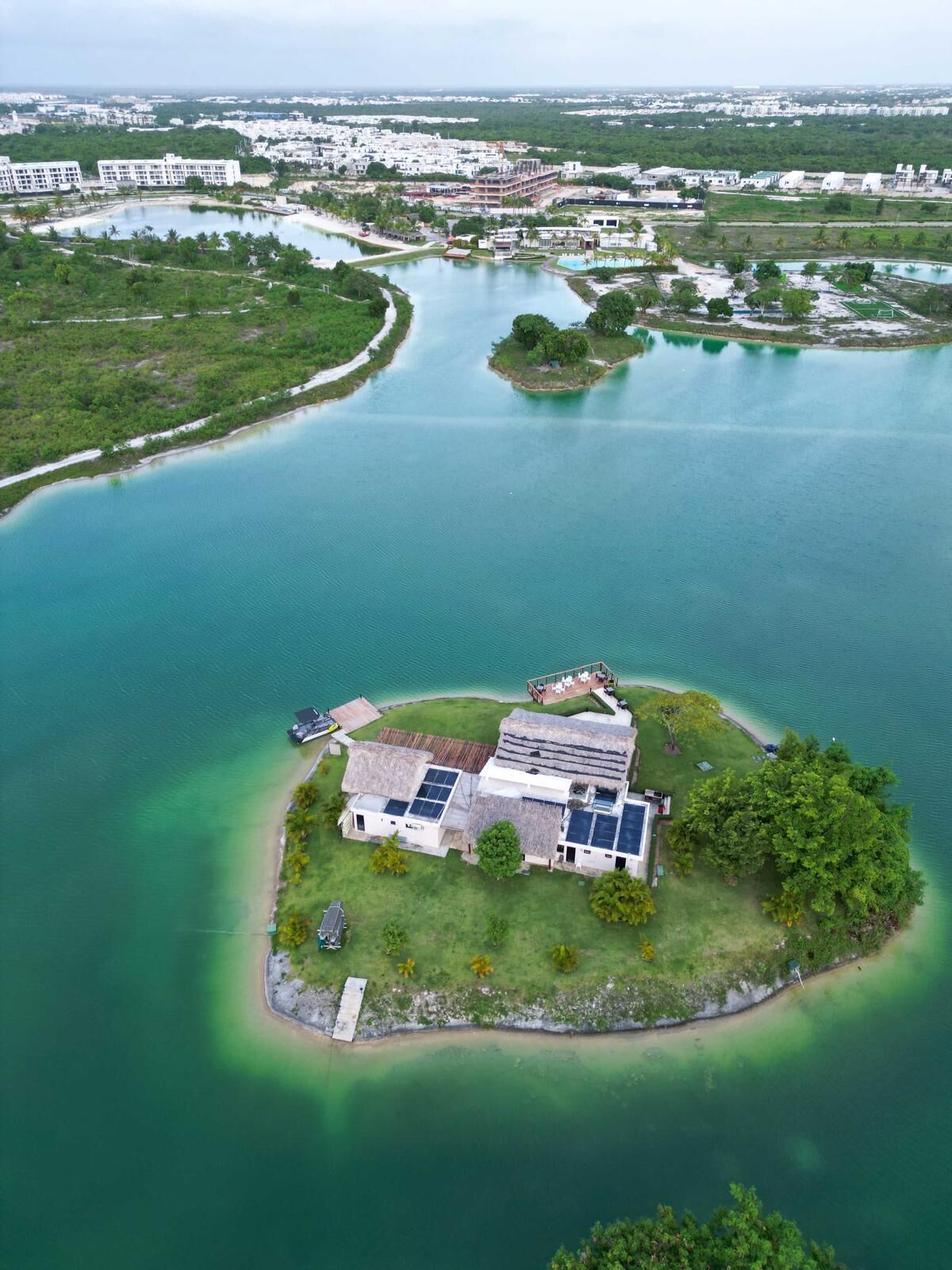 Una vista aerea di una proprietà costiera con una casa circondata da una piccola isola, una vasta distesa d'acqua e una città all'orizzonte.