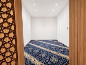 A room with a patterned carpet, white walls, and a wooden door. - AlMohajer Serviced Apartments Airport  (jeddah)