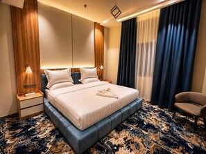 Een moderne hotelkamer met een groot bed, een nachtkastje, een stoel en een kamerbreed tapijt met dessin.