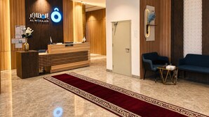 En hotellobby med en receptionsdisk i trä, en röd matta och en blå soffa.