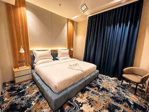 A modern hotel room with a large bed, a nightstand, a chair, and a patterned carpet. - AlMohajer Serviced Apartments Airport  (jeddah)