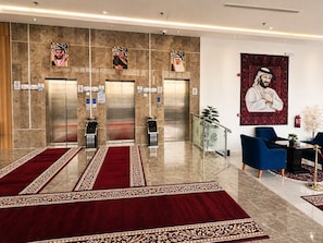 A lobby with three elevators, a red carpet, and a large portrait on the wall. - AlMohajer Serviced Apartments Airport  (jeddah)
