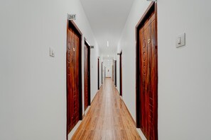 A long, narrow hallway with wooden doors on both sides, numbered signs above each door, and a wooden floor. - Super Collection O Kovur (Chennai)