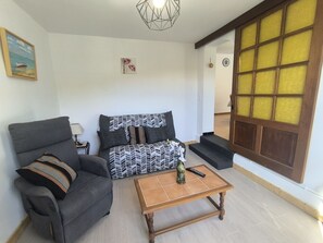 Ein Wohnzimmer mit Sofa, Sesseln, Couchtisch und einem großen Fenster mit Holztür.