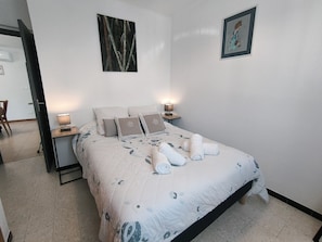Ein ordentlich bezogenes Bett mit einem floralen Überwurf, zwei Nachttischlampen und einem gerahmten Bild an der Wand.