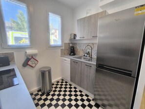 A kitchen with a stainless steel refrigerator, a dishwasher, a sink with a faucet, and a window with a view of a street. - L'OLivier de Romolea 4personnes/jardin classée 3 étoiles (Roumoules)
