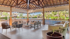 Un espacio lounge al aire libre con mobiliario de mimbre, vista a la piscina y un jardín tropical de fondo.