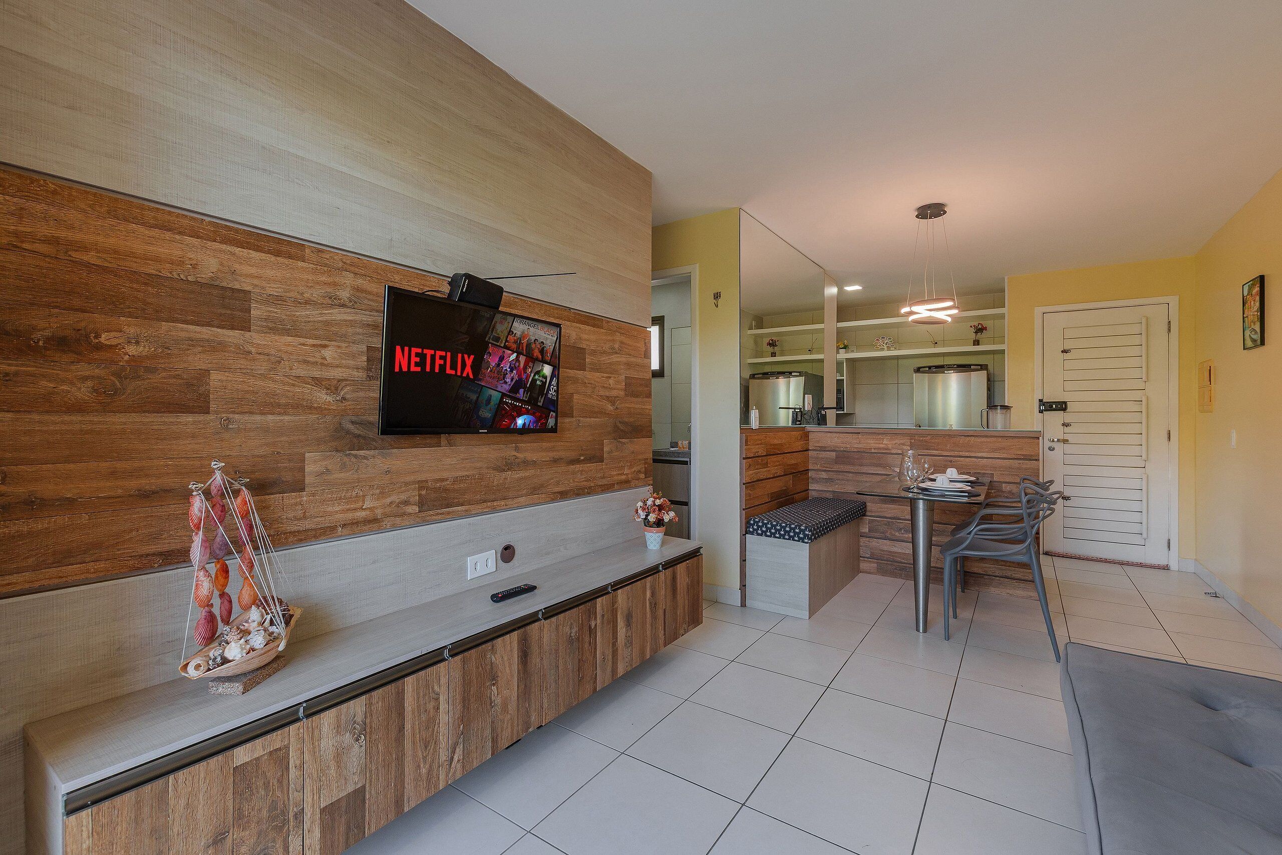 Una cocina moderna con una pared de acento de madera, un televisor integrado y una zona de comedor con mesa y sillas.