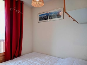Ein Schlafzimmer mit einem Bett, einem roten Vorhang, einem gerahmten Bild an der Wand und einer Pendelleuchte.
