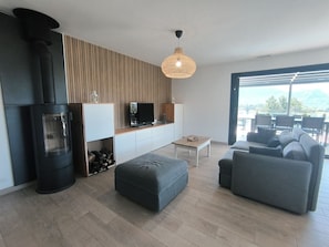 Ein modernes Wohnzimmer mit Kamin, einer Couch, einem Hocker und einem Essbereich mit Stühlen.