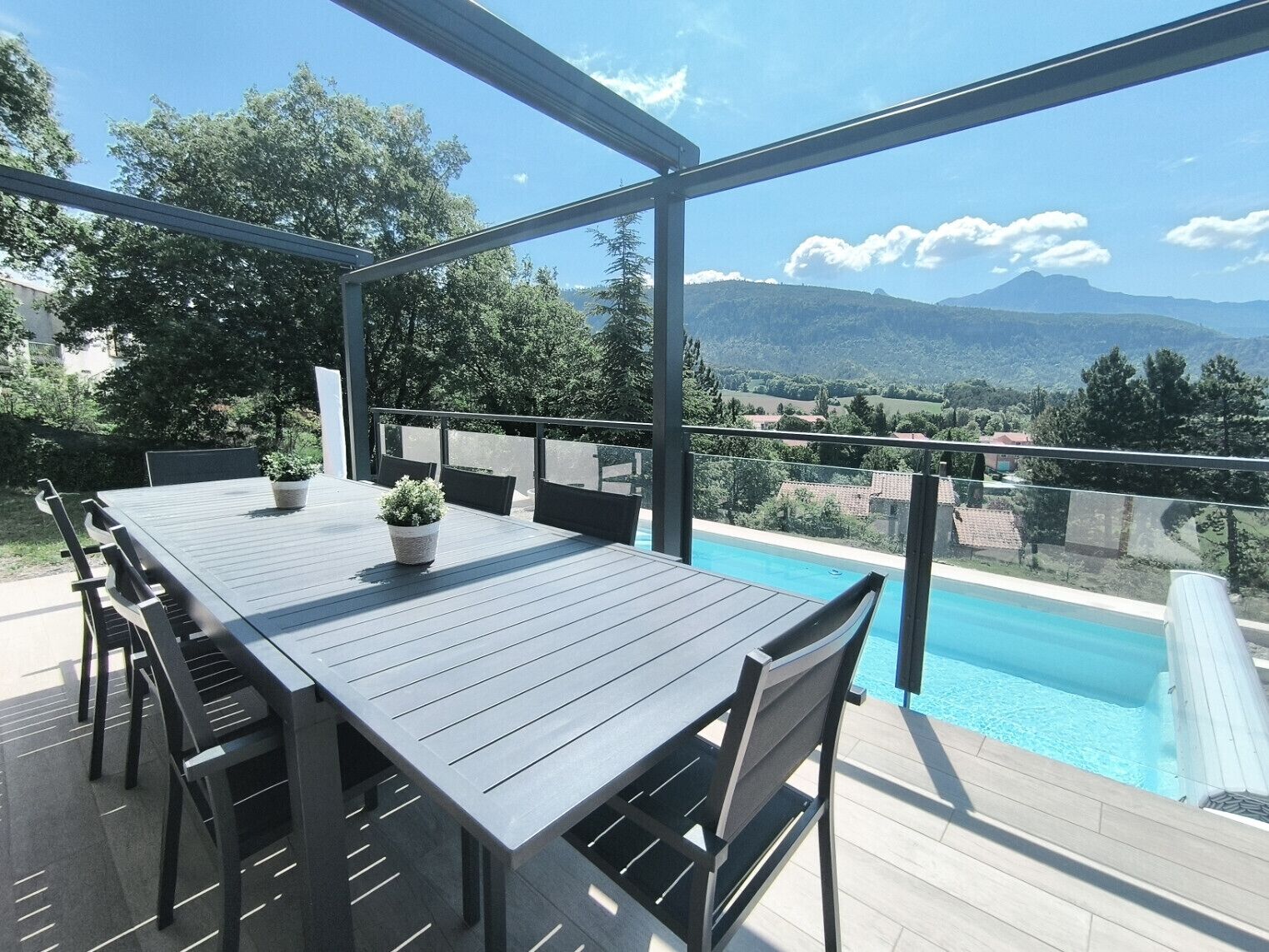 Un espace de restauration en plein air avec une piscine, entouré d’une structure en verre, offrant une vue sur un paysage montagneux.