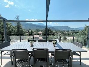 Terraço com mesa e cadeiras, com vista para uma paisagem montanhosa.