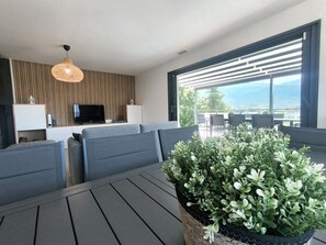 A modern living room with a sofa, a dining table, and a large window with a view of the outdoors.