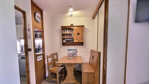 Une table à manger en bois avec des chaises, un buffet en bois contenant de la verrerie, et une horloge au mur.