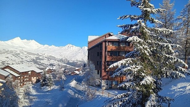 Une station de montagne enneigée, avec un bâtiment moderne, des pistes de ski et des arbres chargés de neige.
