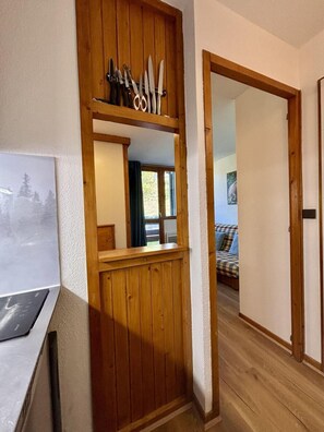 Ein Holzinnenraum mit Küchenzeile, einem Spiegel und einem durchgehenden Türrahmen erkennbaren Schlafzimmer.