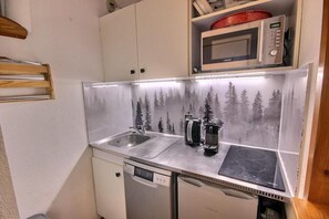 Eine kompakte Küchenzeile mit Spülbecken aus Edelstahl, einer Mikrowelle und einer Kaffeemaschine.