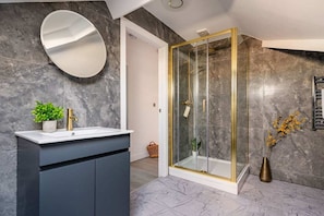 A modern bathroom with a marble wall, a round mirror, a gold shower, and a dark cabinet. - Albemarle Chambers Central Retreat Sleeps 2 (Scarborough)