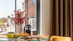 A table with a vase of flowers, a coffee pot, a cup, and pastries.