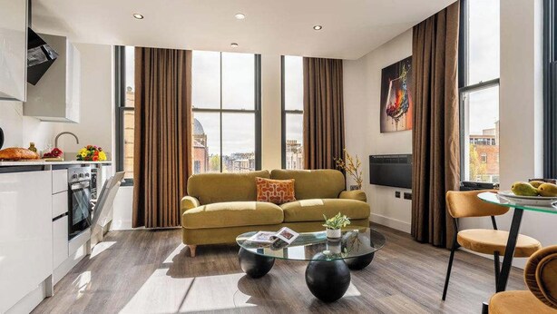 A modern living room with a sofa, a glass coffee table, and a dining area with a chair.