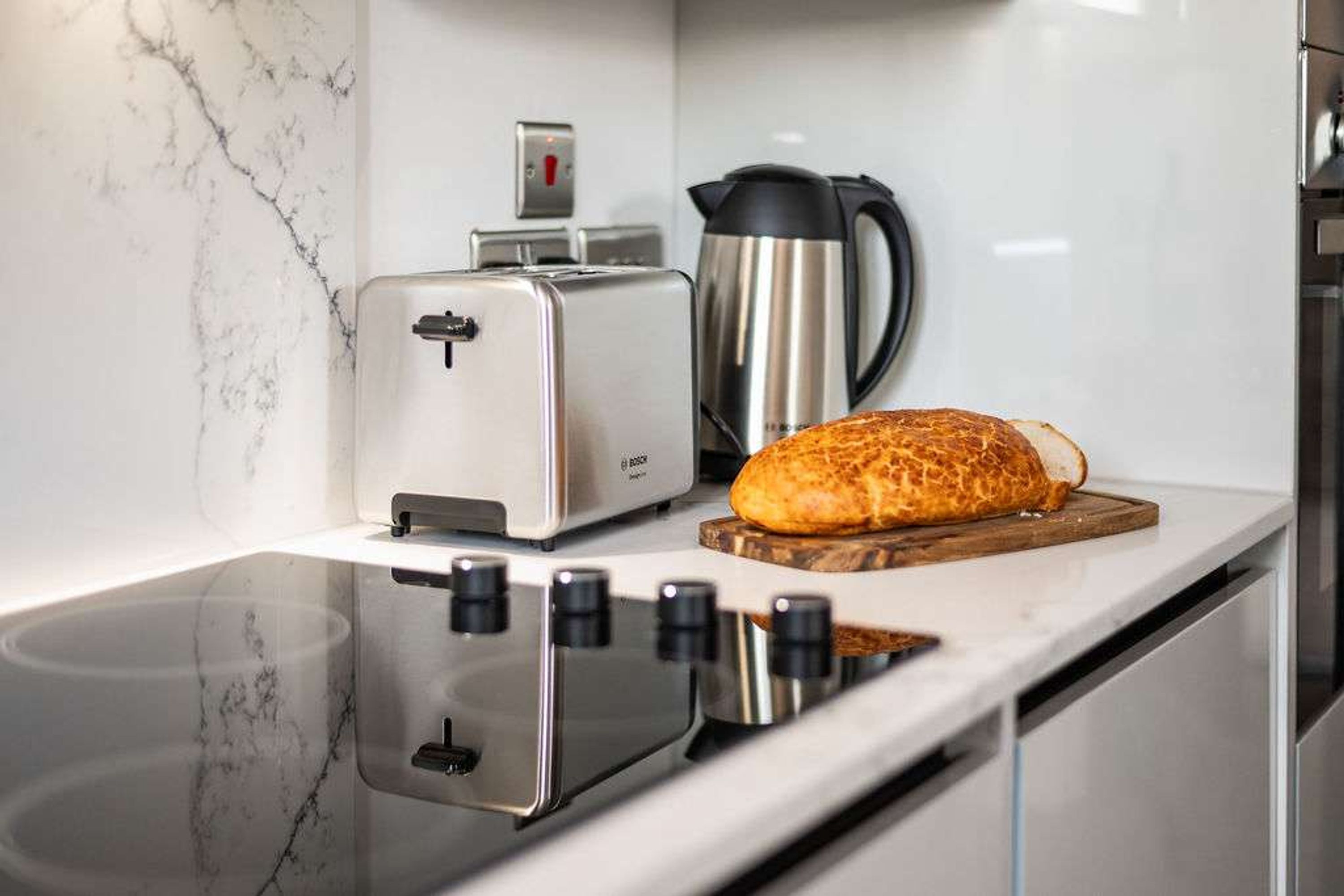 A kitchen with a toaster, a bread loaf on a wooden board, and a coffee maker.