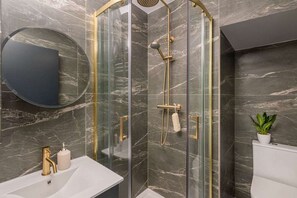 A modern bathroom with a glass-enclosed shower, a round mirror, a white sink, and a potted plant.