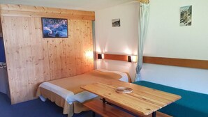 Een kamer met een houten stapelbed, een houten tafel met een bankje en uitzicht op een besneeerd landschap door een raam.