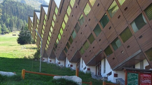 Een rij chalets met een kenmerkend diamantpatroon op het dak, gelegen tegen een bergachtige achtergrond.