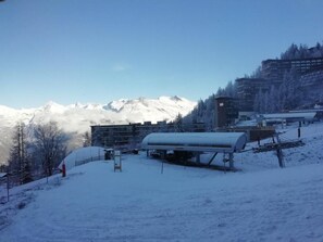 Ein verschneiter Außenbereich mit einem Gebäude, einer großen zylindrischen Struktur und Bergen im Hintergrund.