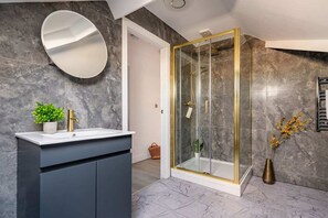 A modern bathroom with a marble wall, a round mirror, a gold shower, and a dark cabinet. - Albemarle Chambers Central Retreat Lift Sleeps 2 (Scarborough)