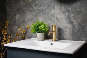 Un baño con un lavamanos blanco, un grifo dorado y una planta en maceta.