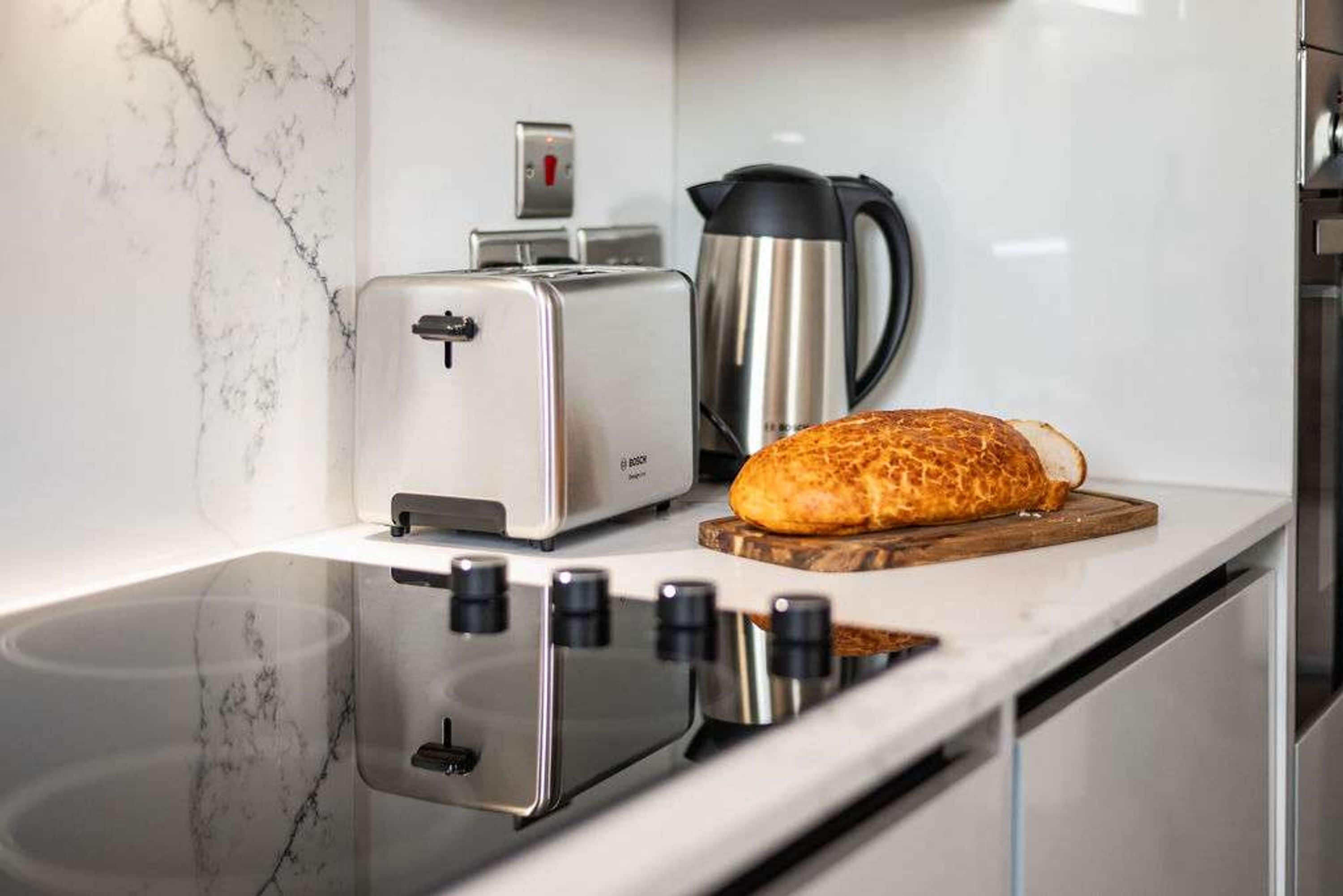 A kitchen with a toaster, a bread loaf on a wooden board, and a coffee maker.