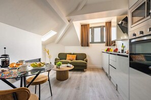 Una cocina moderna con horno integrado, un comedor con mesa de vidrio y una sala de estar acogedora con sofá y ventana.