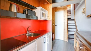 Een kleine keuken met een rode aanrecht, een roestvrijstalen spoelbak en een magnetron.
