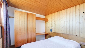 Een kamer met houten lambrisering, een bed, een klein tafeltje en een wandlamp.