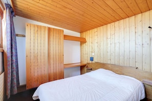 Ein Zimmer mit Holzwänden, einem Bett, einem kleinen Tisch und einer Wandleuchte.