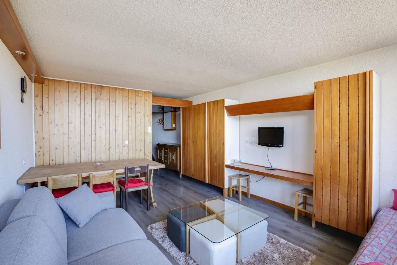 Een moderne woonkamer met een houten eettafel, een bank, een glazen salontafel en een aan de muur bevestigde televisie.