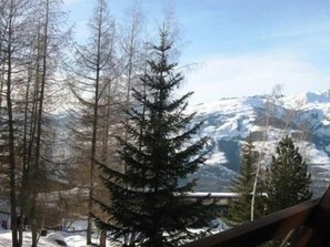 Eine Berglandschaft mit schneebedeckten Gipfeln und kahl stehenden Bäumen.