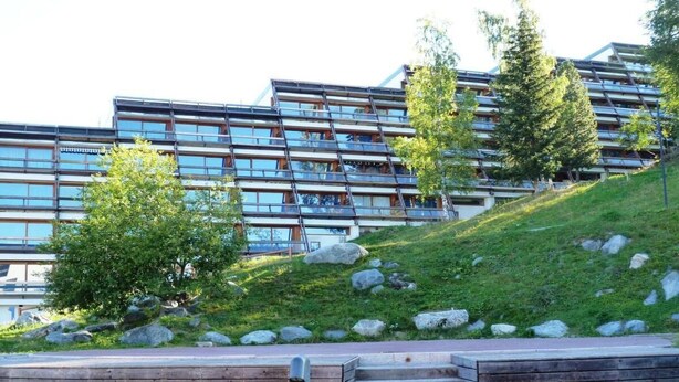 A modern building with a sloped roof and multiple windows. There is a grassy area with trees and rocks in front of the building. - 50m from ski slopes, 1st floor, balcony, tv, 30m², Les Arcs (Les Arcs)