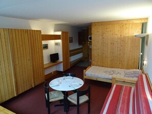 Ein kleiner Raum mit rundem Tisch, zwei Stühlen, einem Einzelbett und einer kleinen Couch.