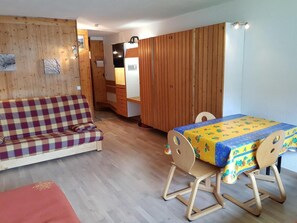 A cozy room with a sofa, a dining table with a colorful tablecloth, wooden walls, and a kitchenette in the background. - 50m from resort center, 3rd floor, tv, 34m², Les Arcs (Les Arcs)