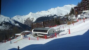 Ein Skigebiet mit schneebedecktem Berg im Hintergrund, einer überdachten Sesselbahnstation und einem mehrstöckigen Gebäude.