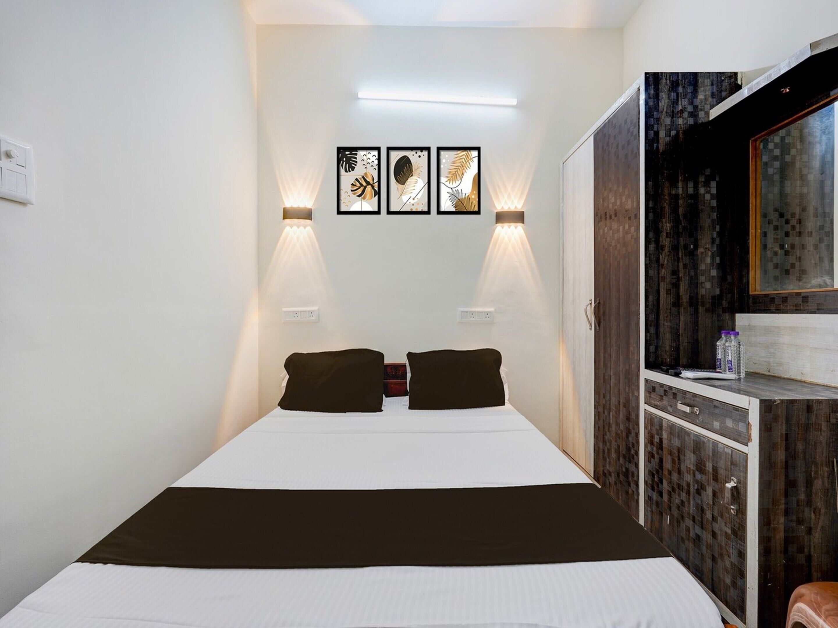 A hotel room with a bed, two wall-mounted lights, and three framed artworks.