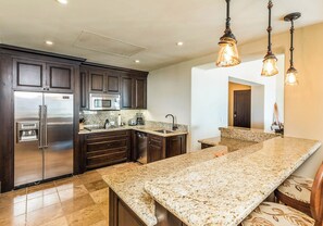 Uma cozinha moderna com armários de madeira escura, eletrodomésticos de aço inoxidável, bancadas de granito e iluminação pendente.