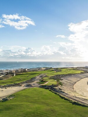 A golf course with a view of the ocean and a building complex in the background. - 2-bedroom Presidential Condo at the Dunes Club in Diamante Cabo San Lucas (Cabo San Lucas)