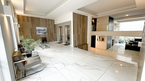 A spacious lobby with marble flooring, a seating area with chairs and a coffee table, a wooden accent wall, and a view of the outside. - Modern and comfortable apartment | WIFI | Air conditioning (Santiago)