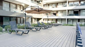A deck with sun loungers and umbrellas, surrounded by a building with multiple balconies and large windows. - Modern and comfortable apartment | WIFI | Air conditioning (Santiago)