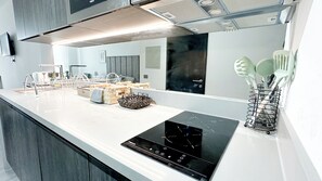 A modern kitchen with a black induction cooktop, a white countertop, and a stainless steel sink. - Modern and comfortable apartment | WIFI | Air conditioning (Santiago)