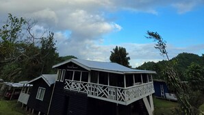 En tvåvåningsbyggnad med en balkong, omgiven av träd och under en delvis molnig himmel.